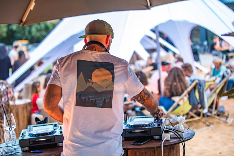 DJ beim Auflegen, dahinter Gäste in Liegestühlen unter den Sternzelten