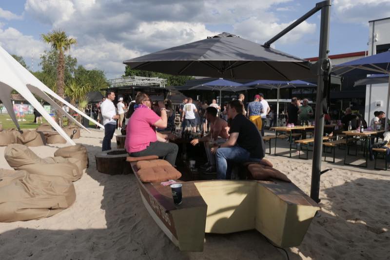 Gäste im Sandbereich rund um das Holzboot als Sitzbank