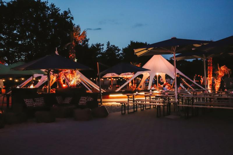 Beach-Bereich bei Nacht mit beleuchteten Zelten und Biertischen